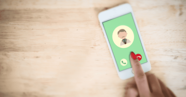 Oak wood desk top with an iphone that has an incoming call on a green background and a finger selecting the red reject button