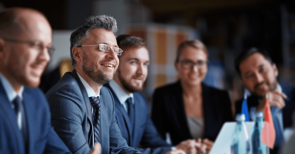 Five business people sitting at a conference table biscussing return on investment with a laptop in front of them