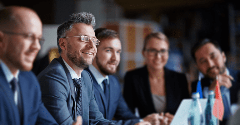 Five business people sitting at a conference table biscussing return on investment with a laptop in front of them