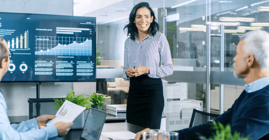 Salesperson wearing black presenting sales forecast to two sales managers in an office on a flat screen television