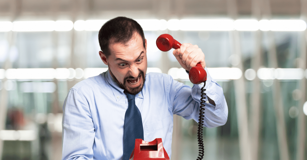 Angry sales person wearing a shirt and tie slamming down a red phone after a cold call prospect hung up on him in an office